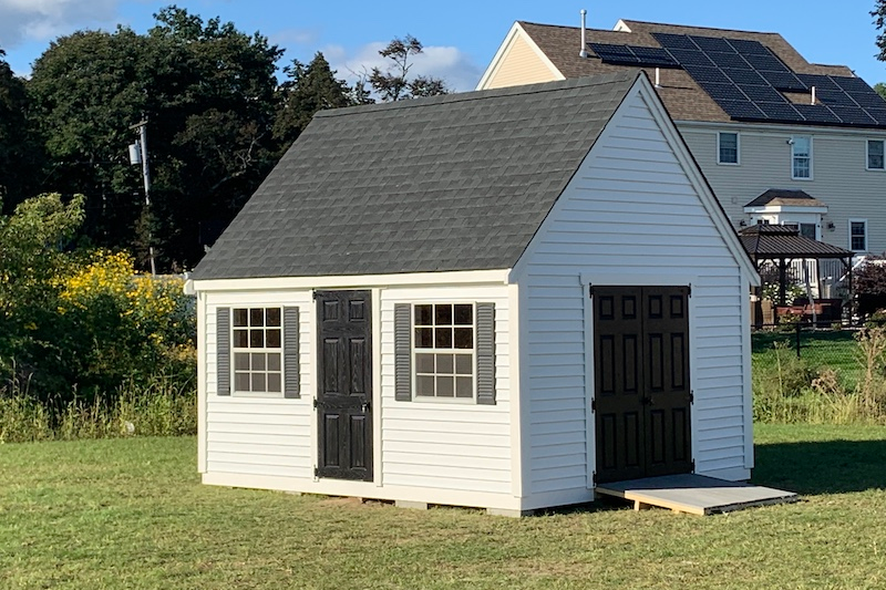 planning and preparation for installing a backyard shed on your property - white shed with windows, two doors, and a black roof with a home in the background