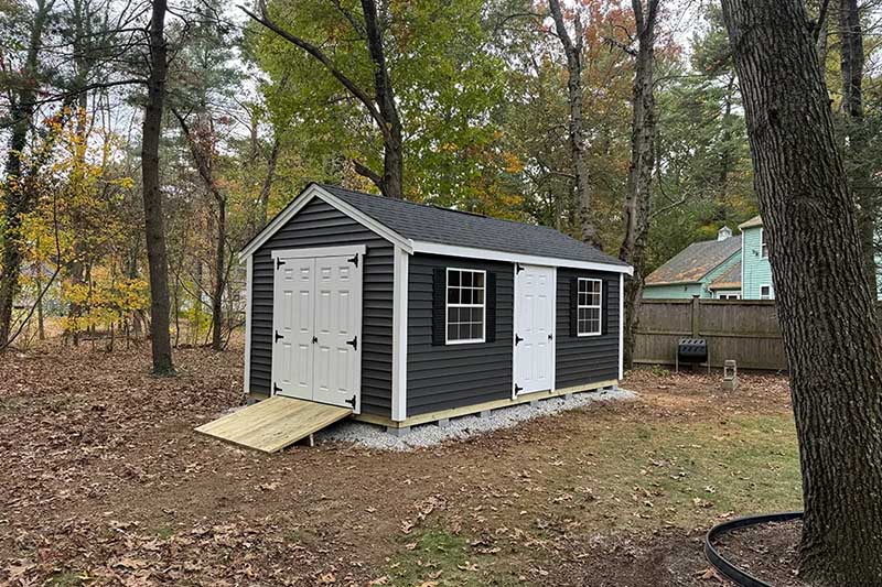 garage door shed - dark shed with entry door, two windows and garage door ramp access in the woods surrounded by trees and on a slab