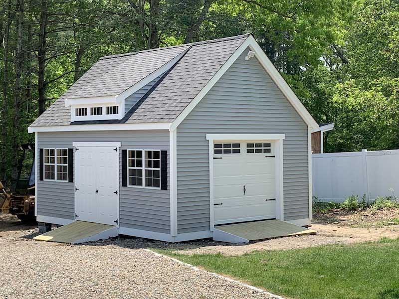 large, gray backyard shed with french doors and a ramp, as well as a garage style door, windows and a vented loft area upstairs