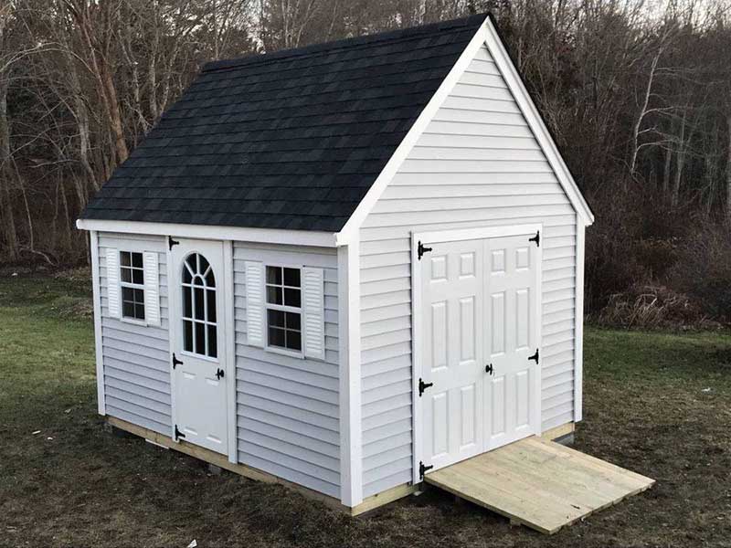 large white shed with windows, a garage door, standard door with a window and a dark roof