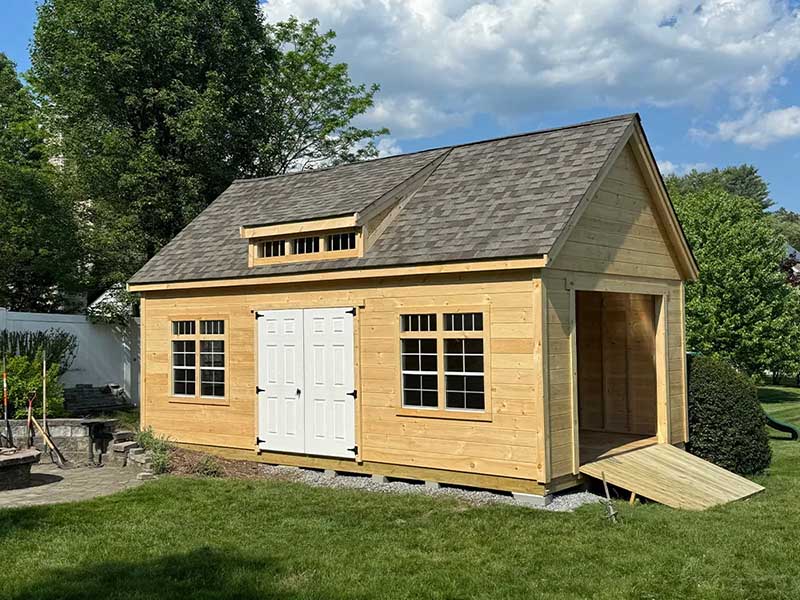 large wooden backyard shed with a garage door and ramp, as well as a double-door entry
