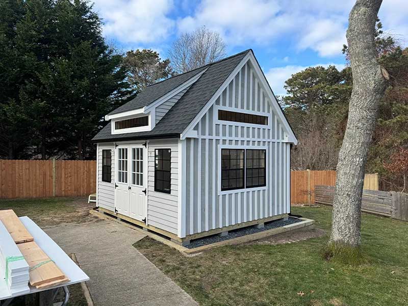 medium sized shed in the process of being installed - white with a black roof and custom siding